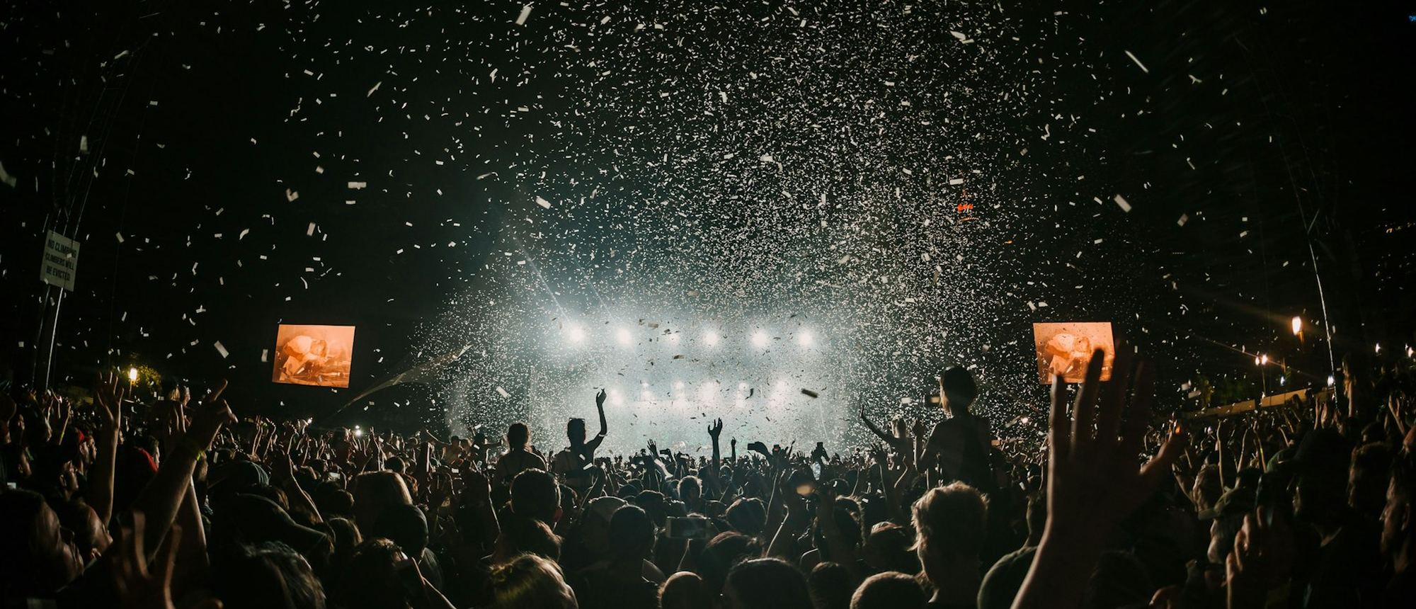 A floodlit event crowd under falling confetti